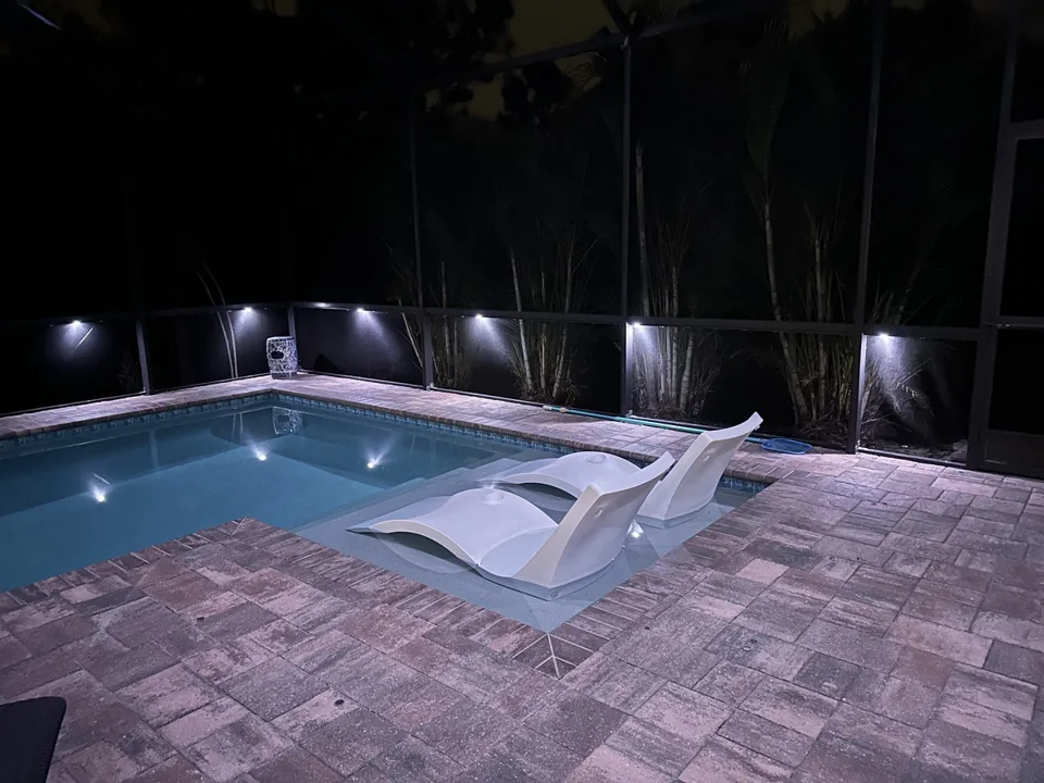 Pool cage lit in warm white over the pool